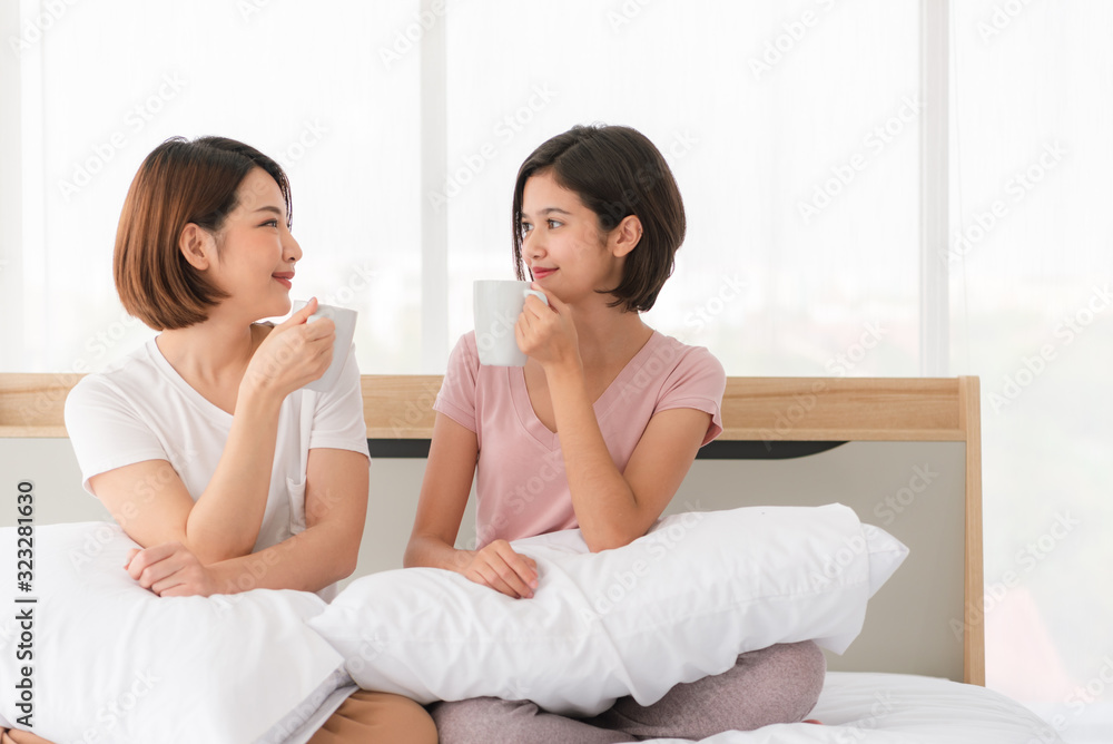 Relaxed young female friends with coffee cups gossiping in bed at home Relaxed young female friends with coffee cups gossiping in bed at home