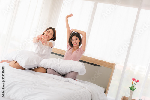 Asian young sisters lovely couple sitting on white bed and holding hands together in bedroom.