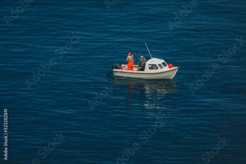 Three lonely fishermen in a plastic white boat on a blue sea water close to the shores of the isle of skye, scotland.