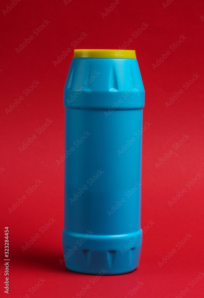 Blue plastic bottle of powder for cleaning on a red background.