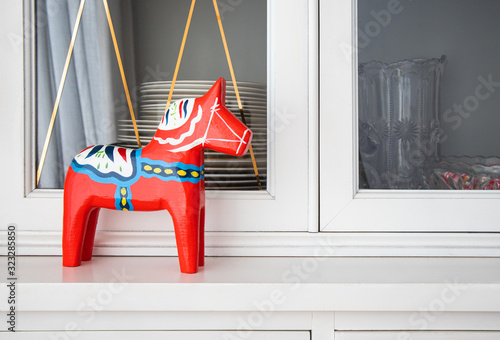 Dalecarlian horse (Dalahäst). Red hand painted wooden statue of a horse in front of white sideboard or buffet with dishes. Dinning room decoration. Symbol of Sweden. photo