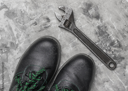 Leather work boots and wrench on gray concrete background. Top view photo