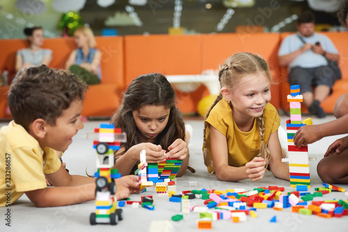 Group of children playing toy blocks. Four little friends in playroom. Happy time together in entertainment center.