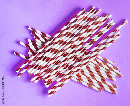 Top view of colorful paper disposable eco-friendly straws. Drinking straws with red strips for party on purple background with copy space. Eco waste concept photo