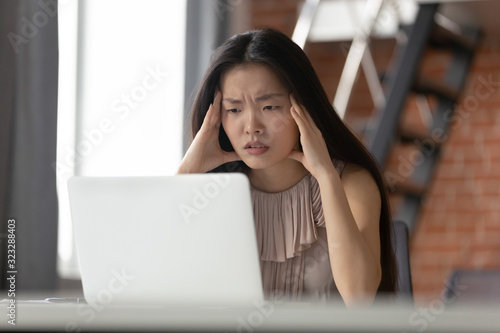 Pensive Asian woman work on laptop think of problem solution