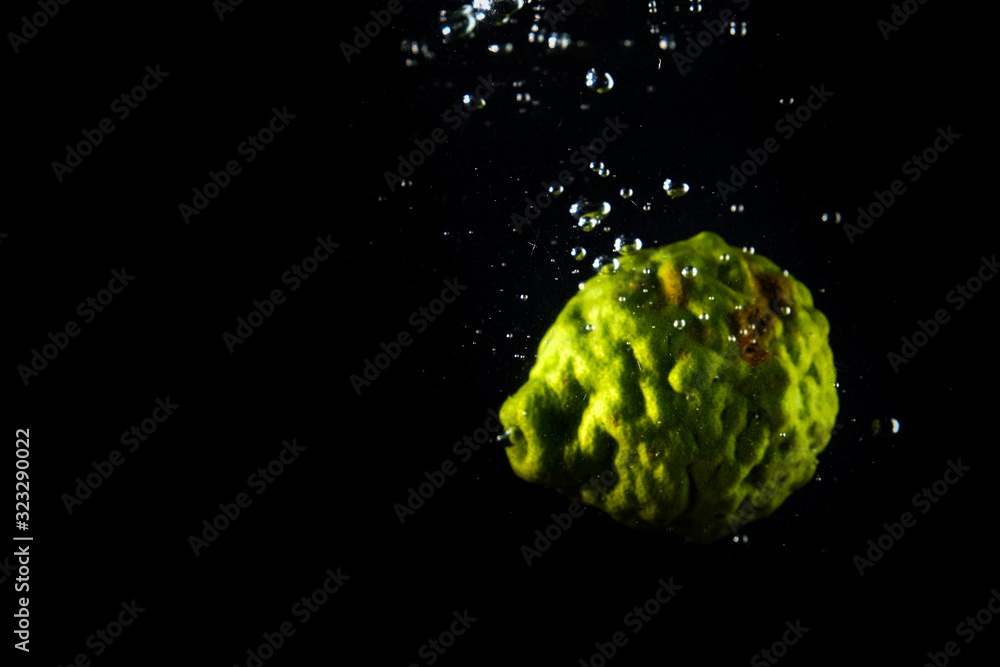 bergamot falling into the water in black background - obrazy, fototapety, plakaty 