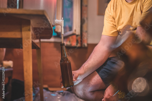 Home craft beer brewery. Final step of pouring a fresh IPA beer into a bottle from fermenter. Hand holding a bottle with home made pale ale beer. photo