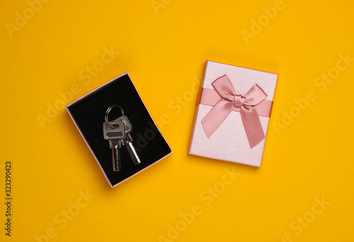 House keys in a gift box with a bow on a yellow background. Housing as a gift. Top view