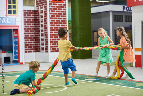 Group of happy children playing tug of war indoor. Gaming room interior with playing kids. Kids amusement park. photo