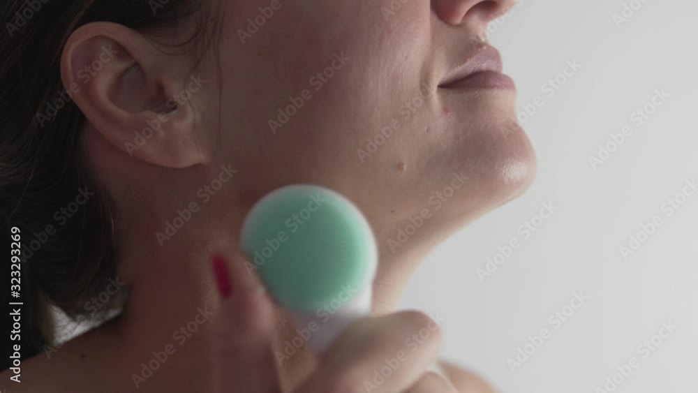 Woman massages facial skin with a massage brush with cream Woman massages facial skin with a massage brush with cream