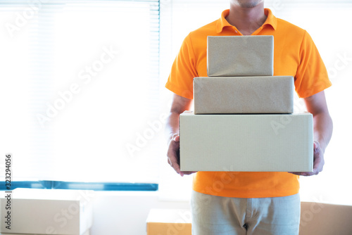 Young delivery asian man in uniform holding and carrying stack of cardboard postel in office. photo