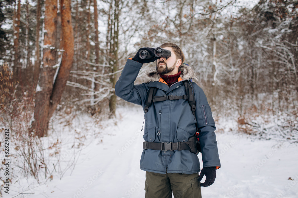 Tourist ranger in fur hood anorak looking into the distance using binoculars Tourist ranger in fur hood anorak looking into the distance using binoculars
