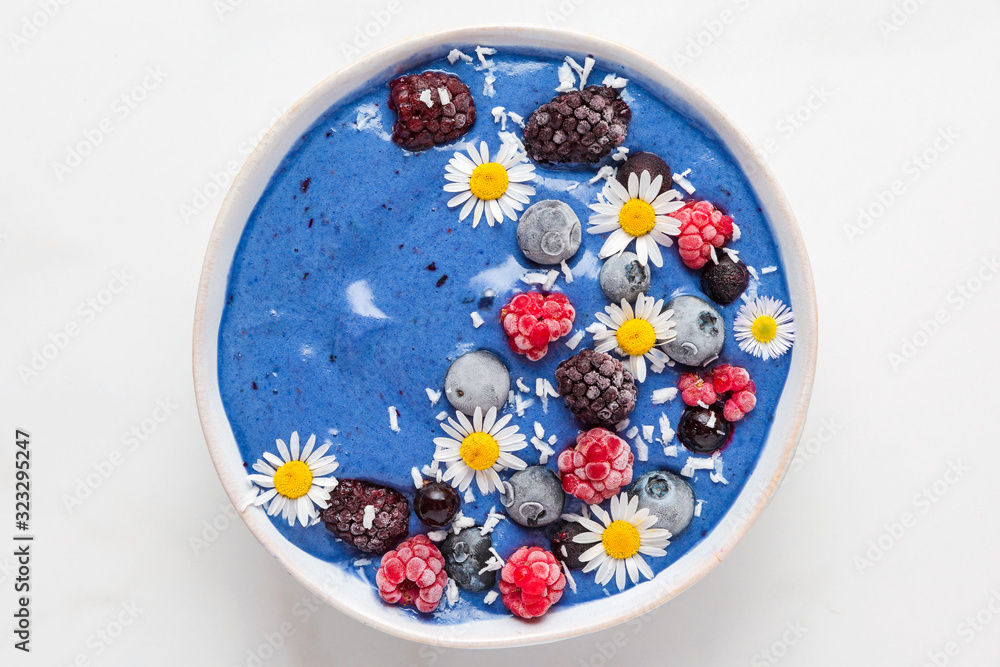 blue spirulina smoothie bowl with fresh and frozen berries, coconut and camomile flowers. healthy breakfast dessert