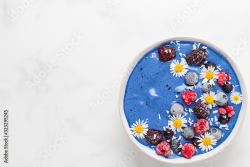 healthy breakfast dessert. blue spirulina smoothie bowl with fresh and frozen berries, coconut and chamomile flowers
