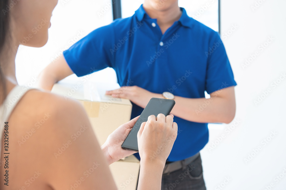 View of young asian woman appending signature in digital smart mobile phone after receiving parcel from courier delivery man at home.AI Technology transportation concept.