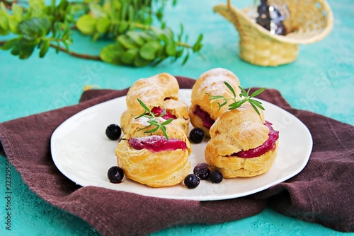 Dessert, choux pastry with cream of cream cheese and blackcurrant berry mousse on a white plate on a turquoise concrete background. Berry Cream Desserts recipe.