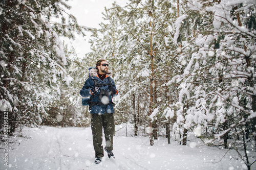 Brown-haired bearded hiker walking through snowfall along winter forest path