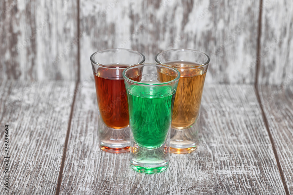 Three shots with different alcoholic beverages stand on a wooden stand Three shots with different alcoholic beverages stand on a wooden stand