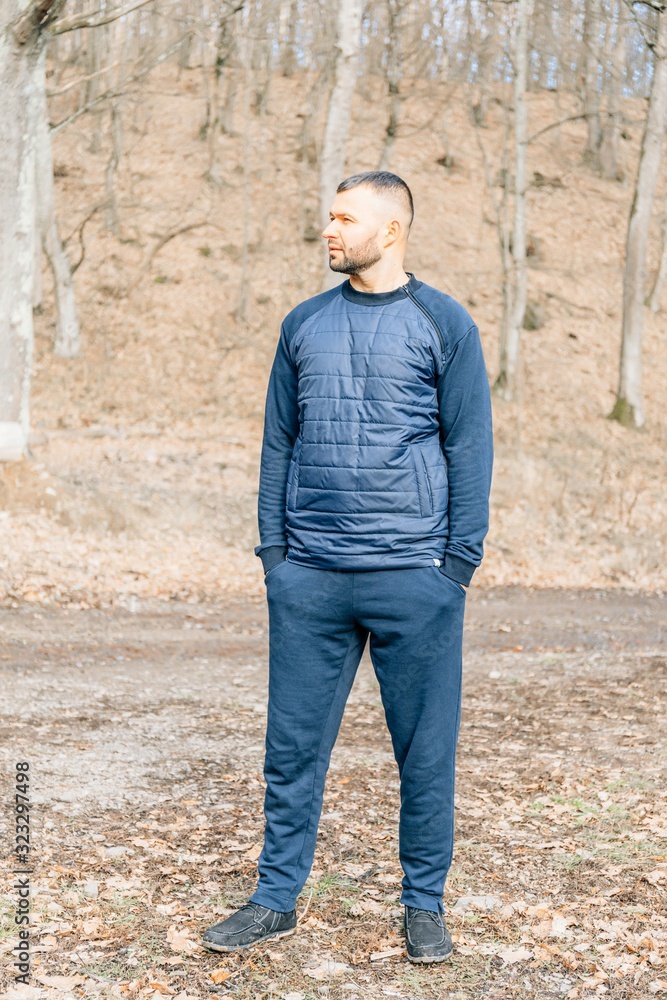 Attractive man with beard is standing in a park at sunset. Stylish Hipster man. Autumn Fashion Look