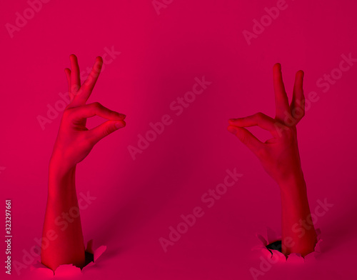 Female hands through the torn holes with pink neon light. Copy space. Creative art