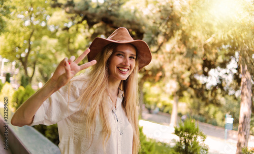 Cheerful blond woman in casual style wearing clothes and felt hat looks into the camera and shows the sign Peas outdoor