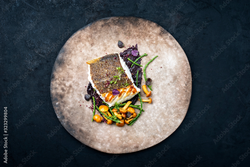 Gourmet fried European skrei cod fish filet with glasswort, fungi and algae as top view on a modern design plate with copy space