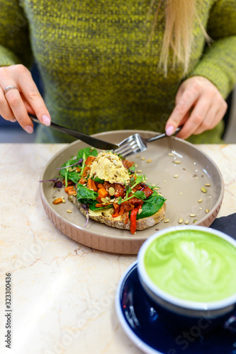 toast with homemade hummus and baked vegetables, matcha latte green tea cup, and woman ready eats. vertical photo