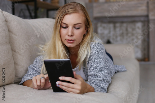 The girl lies on the couch and reads a tablet. Comfortably working remotely at home. Copy space.