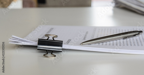 On the table are papers with a clip. Nearby is a silver pen. Concept - business, office