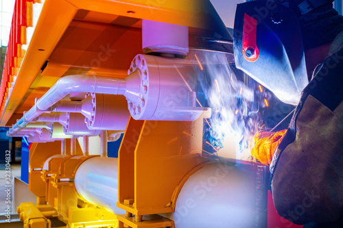 The welder works against a background of yellow pipes. Welding works at the enterprise. Equipment for metal welding. The welder works in the factory shop.