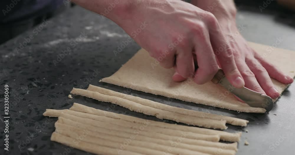 Slow motion man slicing flat dough with knife for making grissini Slow motion man slicing flat dough with knife for making grissini
