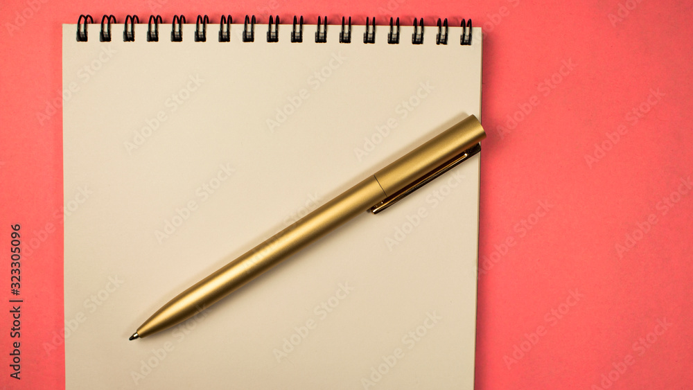 golden pen lies on a notebook on a pink background golden pen lies on a notebook on a pink background