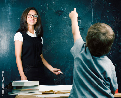 little cute boy in glasses with young real teacher, classroom studying at blackboard school kido photo