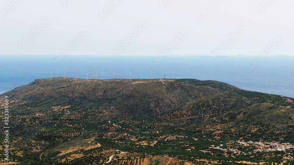 AERIAL: Green mountain with white windmills on top. Turquoise ocean in the background. Crete, Greece AERIAL: Green mountain with white windmills on top. Turquoise ocean in the background. Crete, Greece