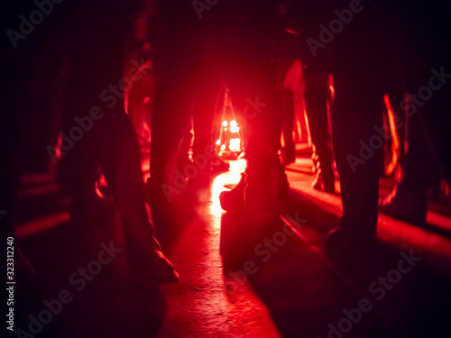Quadro su tela Silhouettes of feet in a nightclub against a bright red lantern in the center wi