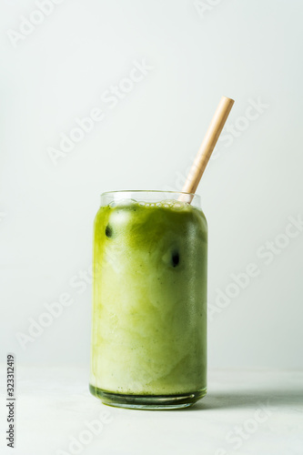 Making Japanese iced matcha latte, green tea with milk, soy milk, traditional matcha tools, with bamboo straw in glass on white background.