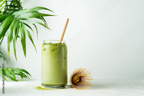 Making Japanese iced matcha latte, green tea with milk, soy milk, traditional matcha tools, with bamboo straw in glass on white background.