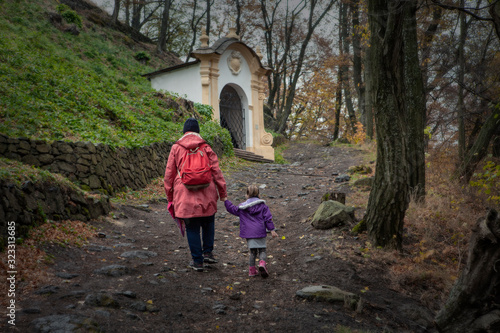 Fototapeta Naklejka Na Ścianę i Meble -  Mother with little doughter rising up the hill on the foothpath to the ruins. Mother with child on the small hike in autumn. Nice fall tour to the ruins of ancient castle.