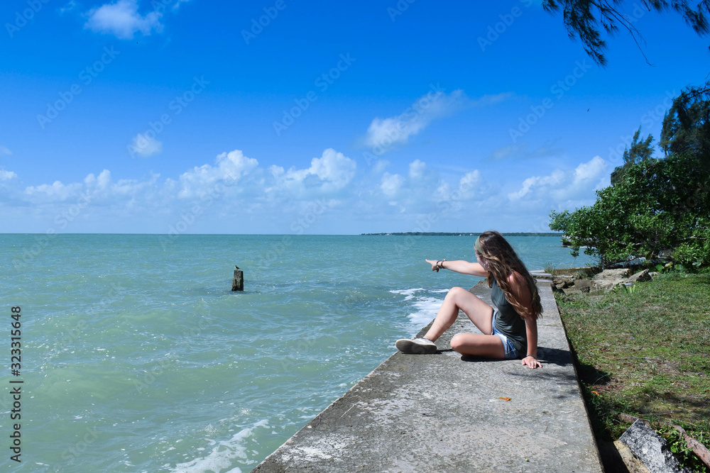 a woman sitting looking out to sea and pointing her finger at the sea