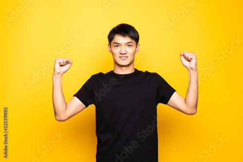 Young asian chinese man celebrating surprised and amazed for success with arms raised and open eyes standing over isolated yellow background . Winner concept.