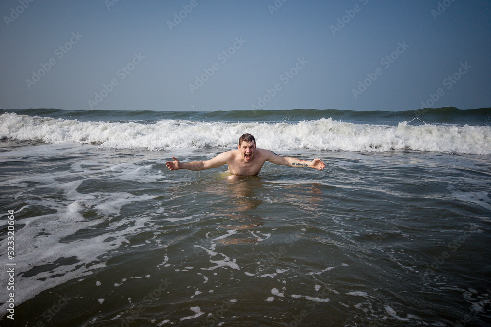 Male in the sea near the coast. Attractive man in sea splashing water and posing to camera. Smiling man having fun in sea water.