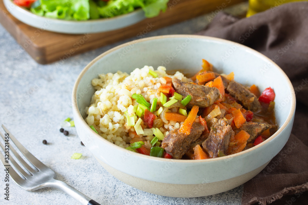Healthy eating concept. Beef stewed with vegetables in bulgur sauce and fresh vegetable salad on a light stone table top. Healthy eating concept. Beef stewed with vegetables in bulgur sauce and fresh vegetable salad on a light stone table top.