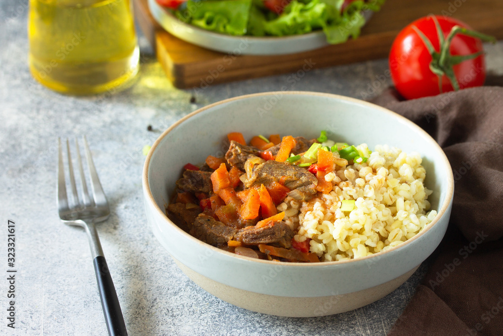 Healthy eating concept. Beef stewed with vegetables in bulgur sauce and fresh vegetable salad on a light stone table top. Healthy eating concept. Beef stewed with vegetables in bulgur sauce and fresh vegetable salad on a light stone table top.