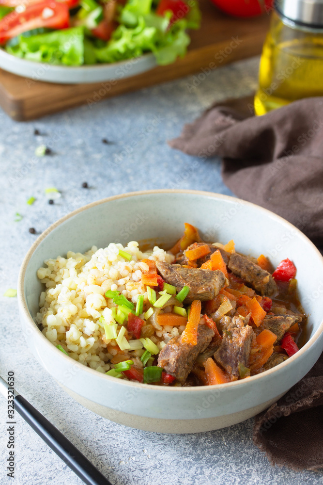 Healthy eating concept. Beef stewed with vegetables in bulgur sauce and fresh vegetable salad on a light stone table top. Copy space. Healthy eating concept. Beef stewed with vegetables in bulgur sauce and fresh vegetable salad on a light stone table top. Copy space.