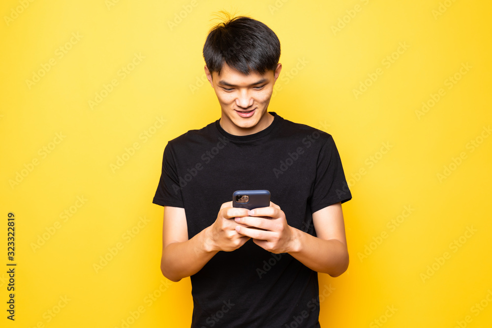 handsome Asian young man using smartphone on studio yellow background handsome Asian young man using smartphone on studio yellow background