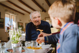 Portrait of old senior man pensioner grandfather sitting at the restaurant looking to his caucasian grandson son boy child taking food family nursery