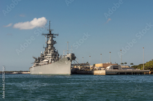 Oahu, Hawaii, USA. - January 10, 2012: Pearl Harbor. Bow of Gray USS Missouri docked and used as historic museum on blue water and under blue cloudscape. Brown buildings on shore. photo