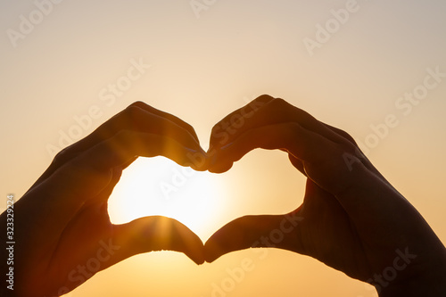 Female hands in the form of heart against the sky pass sun beams. Hands in shape of love heart
