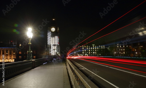 city bridge at night, renovated Big Ben clock in background, colorful trails left by left bus