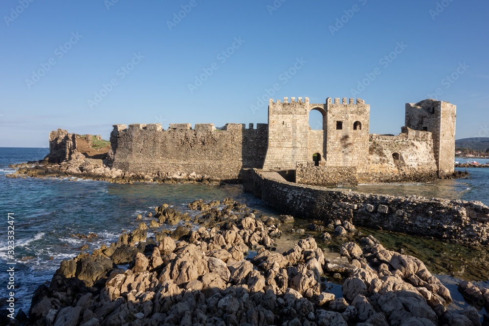 Methoni Castle with a stone bridge in sunny weather during early morning hours with water sea waves and shadows in Greece